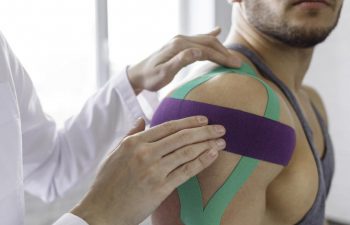 Rehab Specialist Applying Kinesiology Tape Over a Sportsman Shoulder