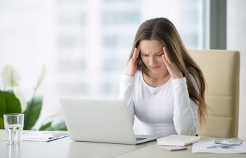 A woman with headache sitting at her office desk.